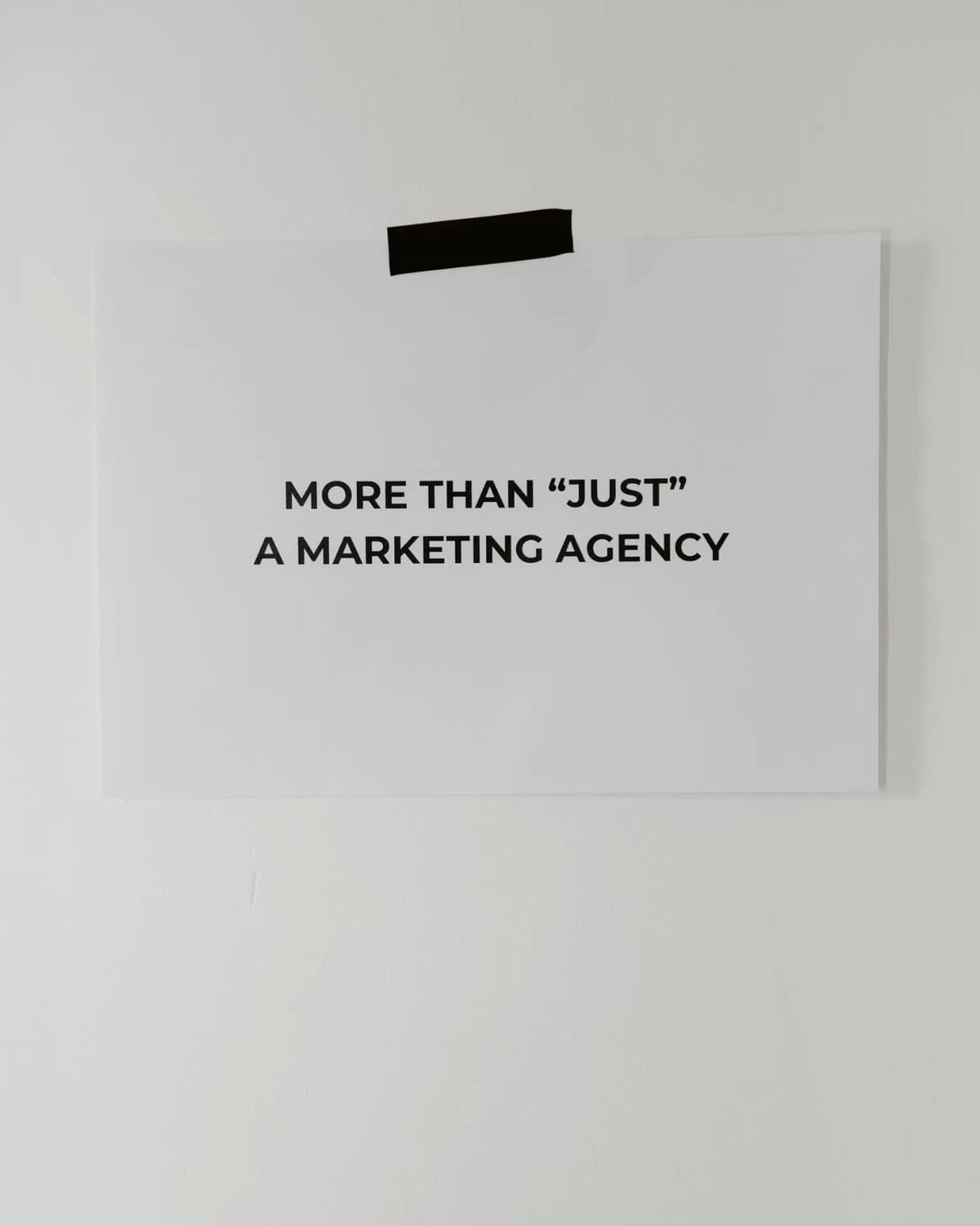 Sheet of paper taped to a white wall reading “More than ‘just’ a marketing agency”